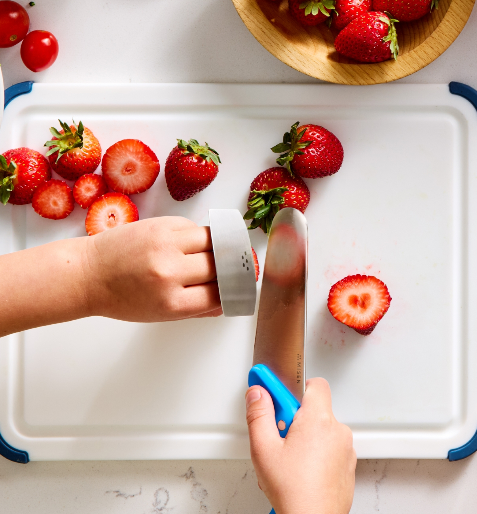 Child safely cutting strawberries on white cutting board using Misen knife with cut-resistant glove