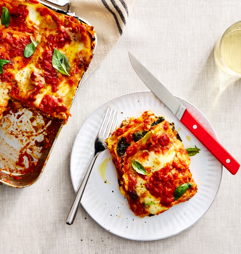 Homemade vegetarian lasagna slice on white plate with tomato sauce, melted mozzarella, and fresh basil